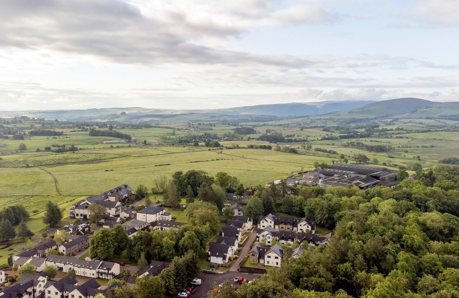 Landal Whitbarrow's stone cottages and lodges among mature trees on the edge of open Cumbrian farmland, with fells along the horizon.