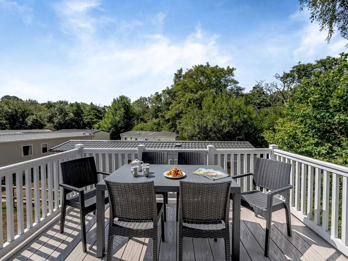 A raised timber deck with a six-seat table and chairs, and trees beyond the white railings.