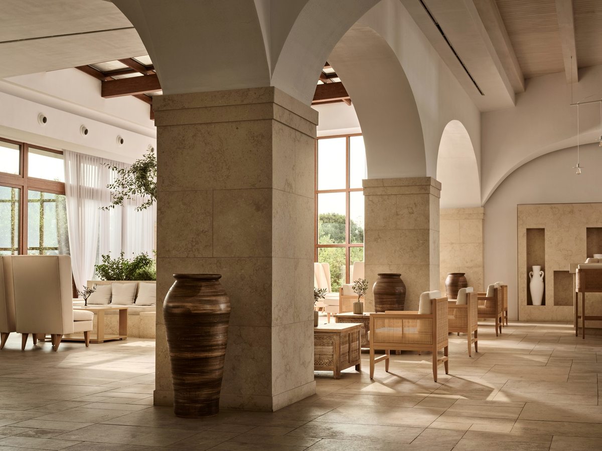 Lounge with tall stone arches, cream armchairs and side tables, large ceramic vases and a pale stone floor.