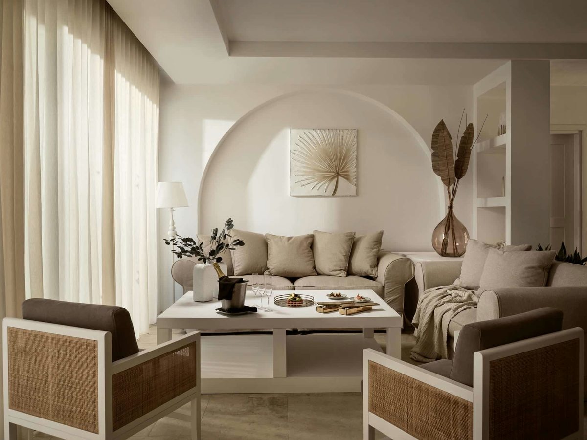 Villa living room with cream sofas, woven armchairs and a low coffee table, set against a curved plaster wall with an arched display niche.