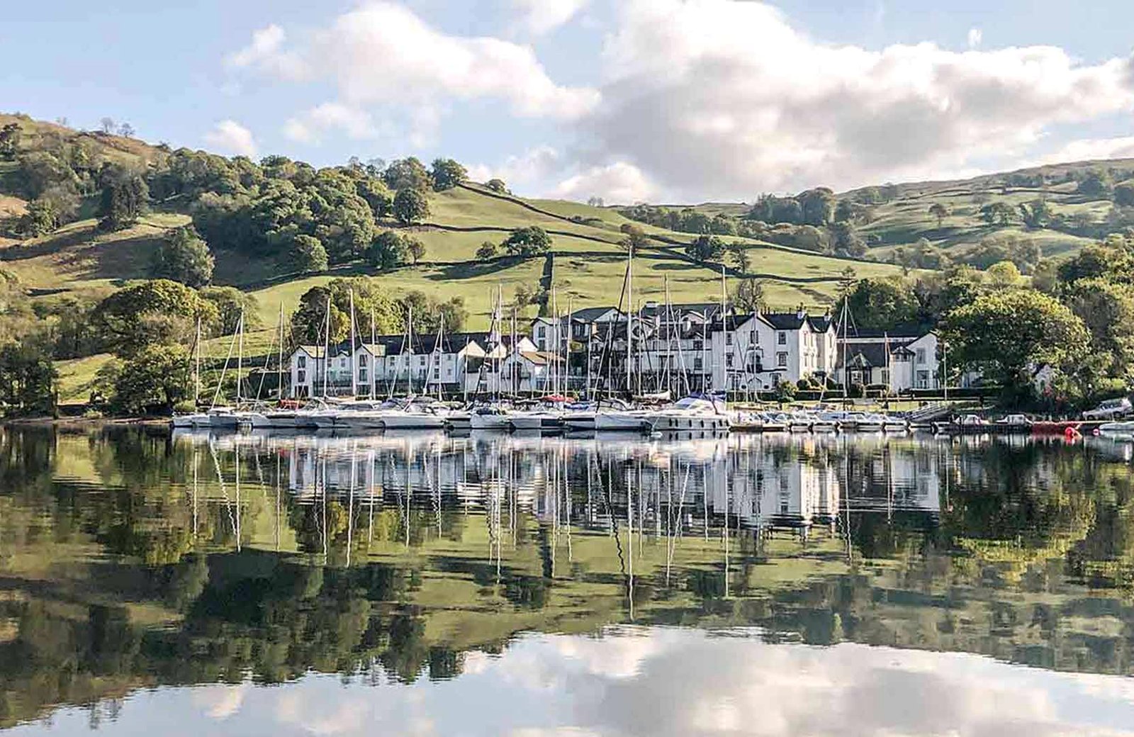 The white buildings of Low Wood Bay Resort & Spa strung along the eastern shore of Lake Windermere, with yachts moored at the marina in front and green fells rising behind.
