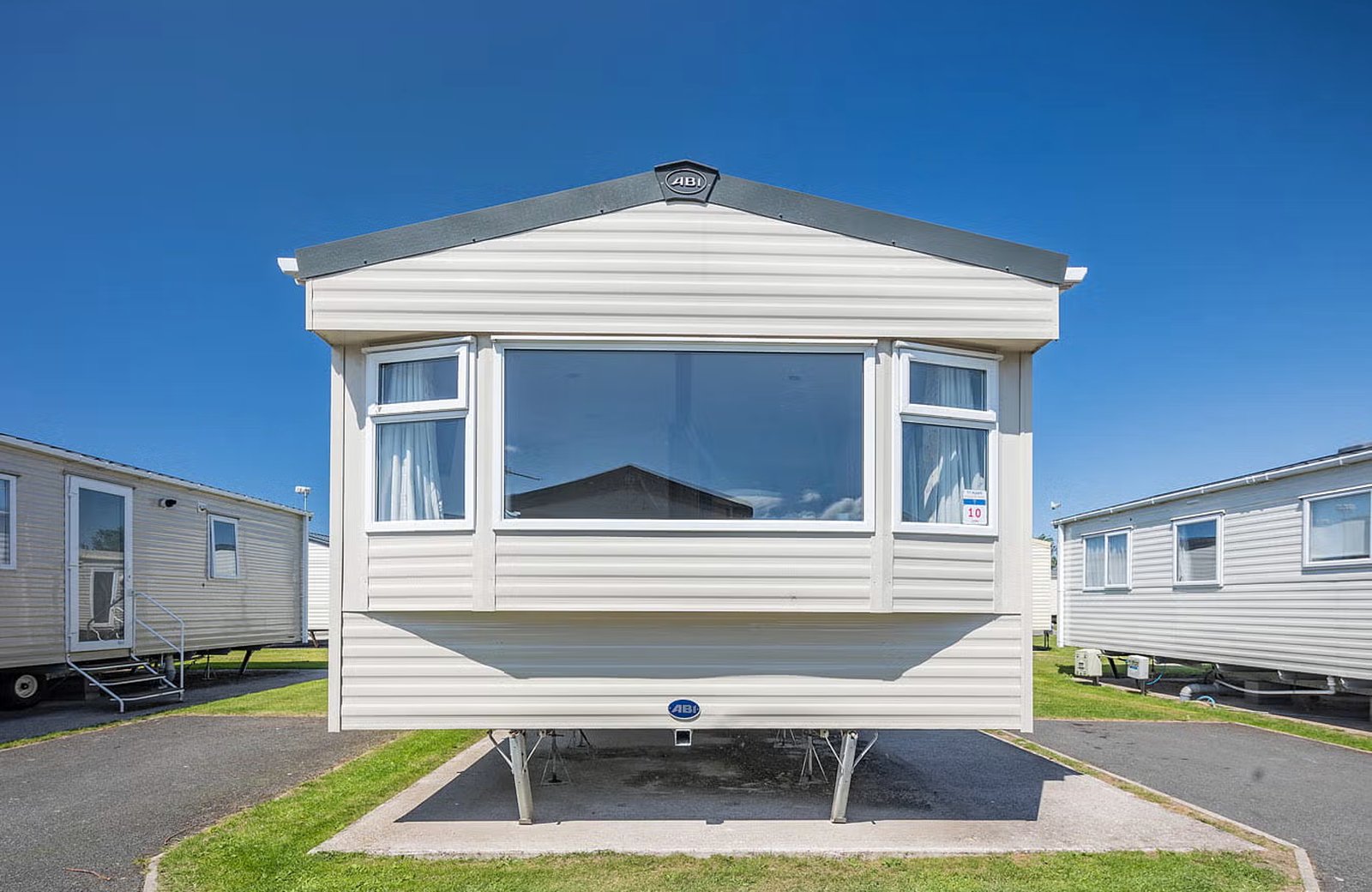 Lower Hyde Holiday Park: a cream static caravan with a wide picture window, standing on a paved pitch under a clear blue sky with neighbouring caravans either side.