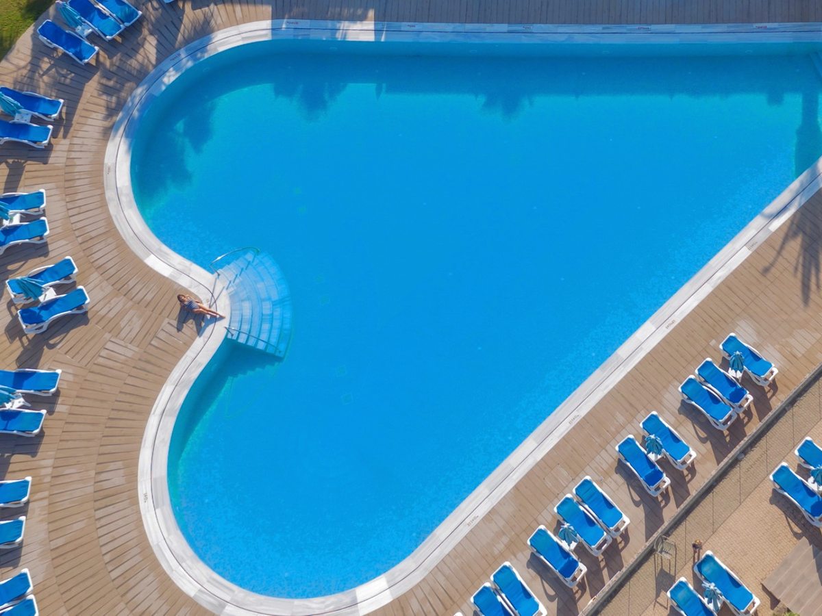 An aerial view of a heart-shaped pool of bright blue water, edged with rows of blue sun loungers.