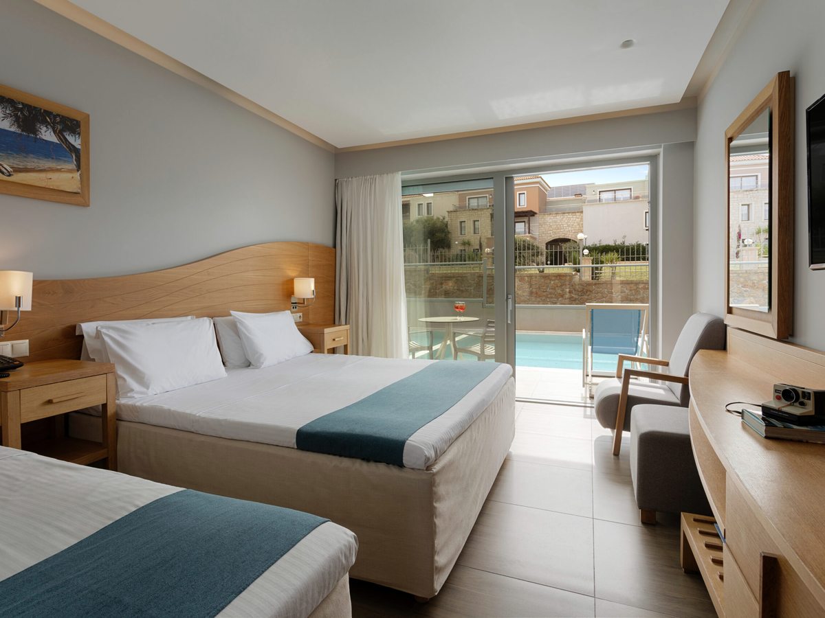 A double bed facing open patio doors, with a terrace and a pool immediately outside.