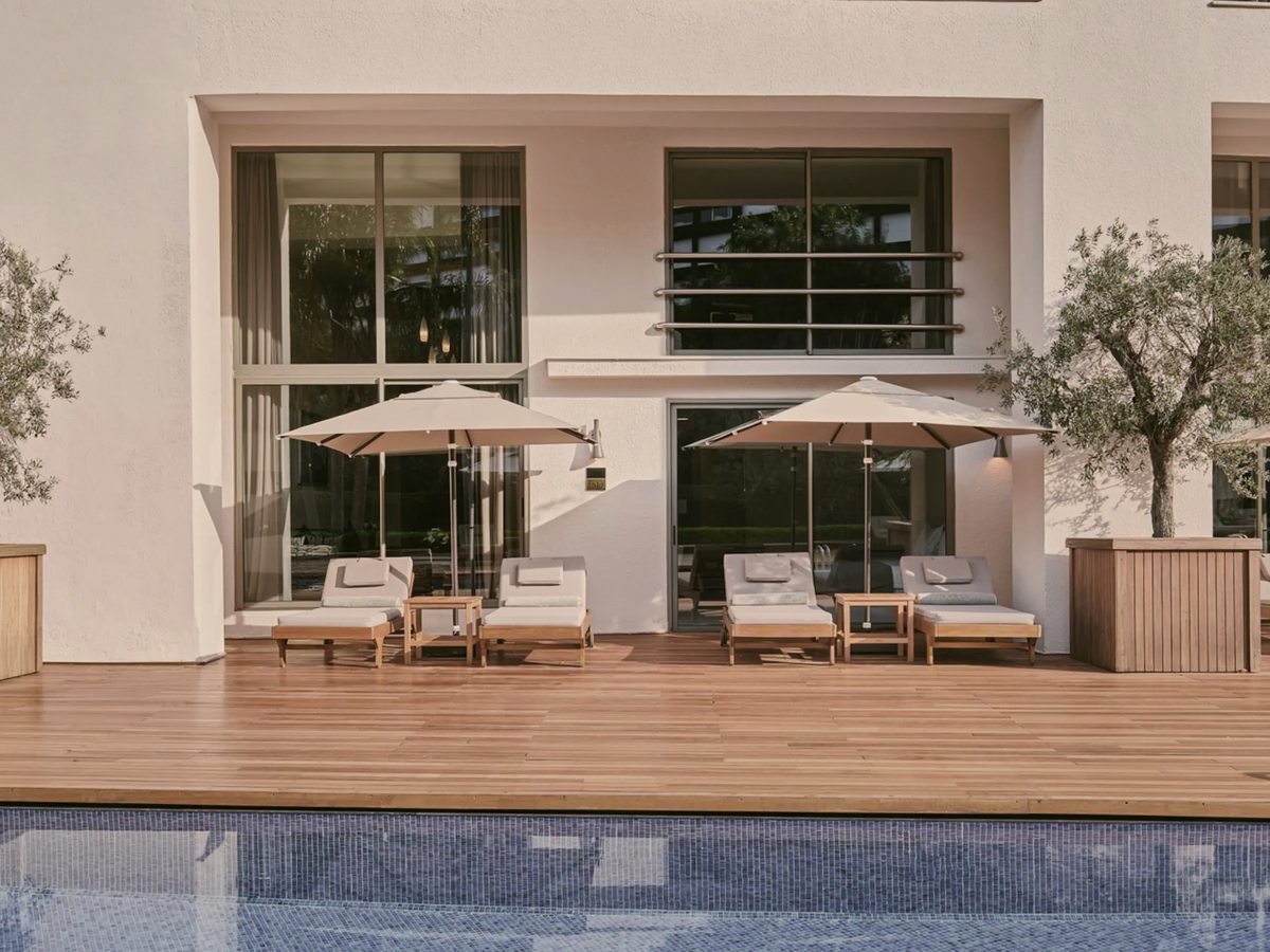 A ground-floor suite with sliding glass doors onto a timber terrace set with sun loungers and parasols, the pool at its edge.