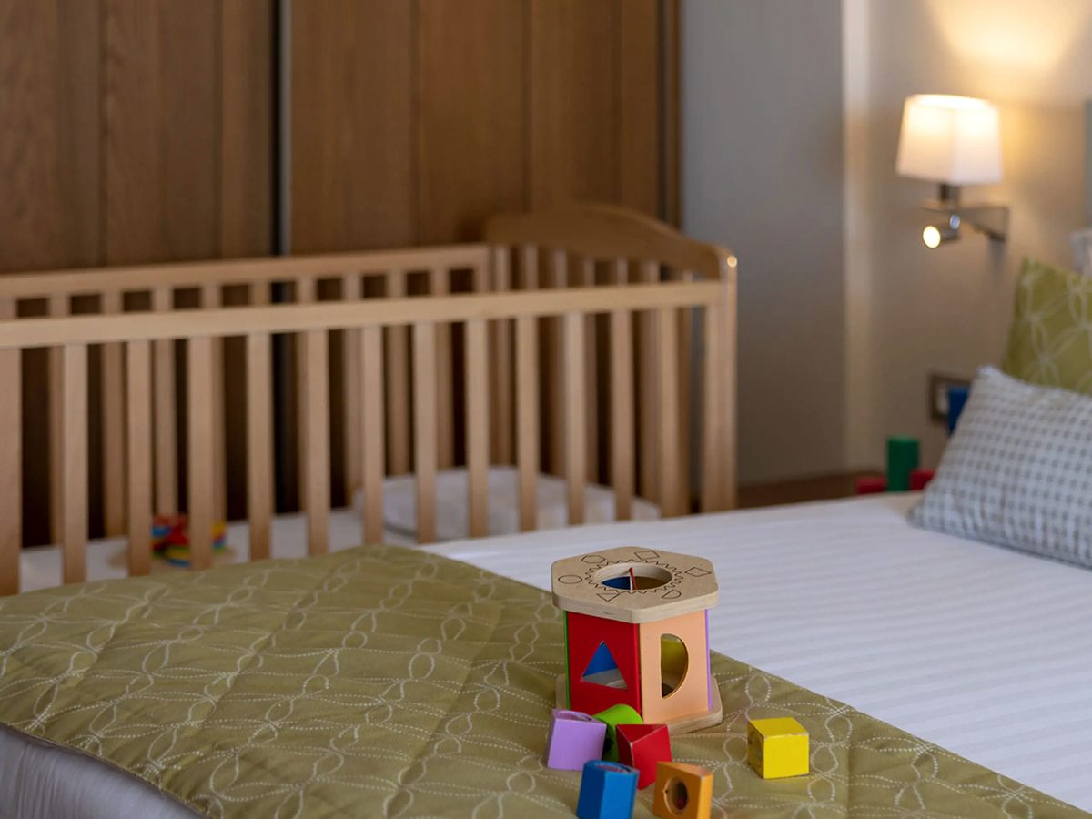 A wooden cot beside a made bed, with a wooden shape-sorter toy and coloured blocks on the bedcover.