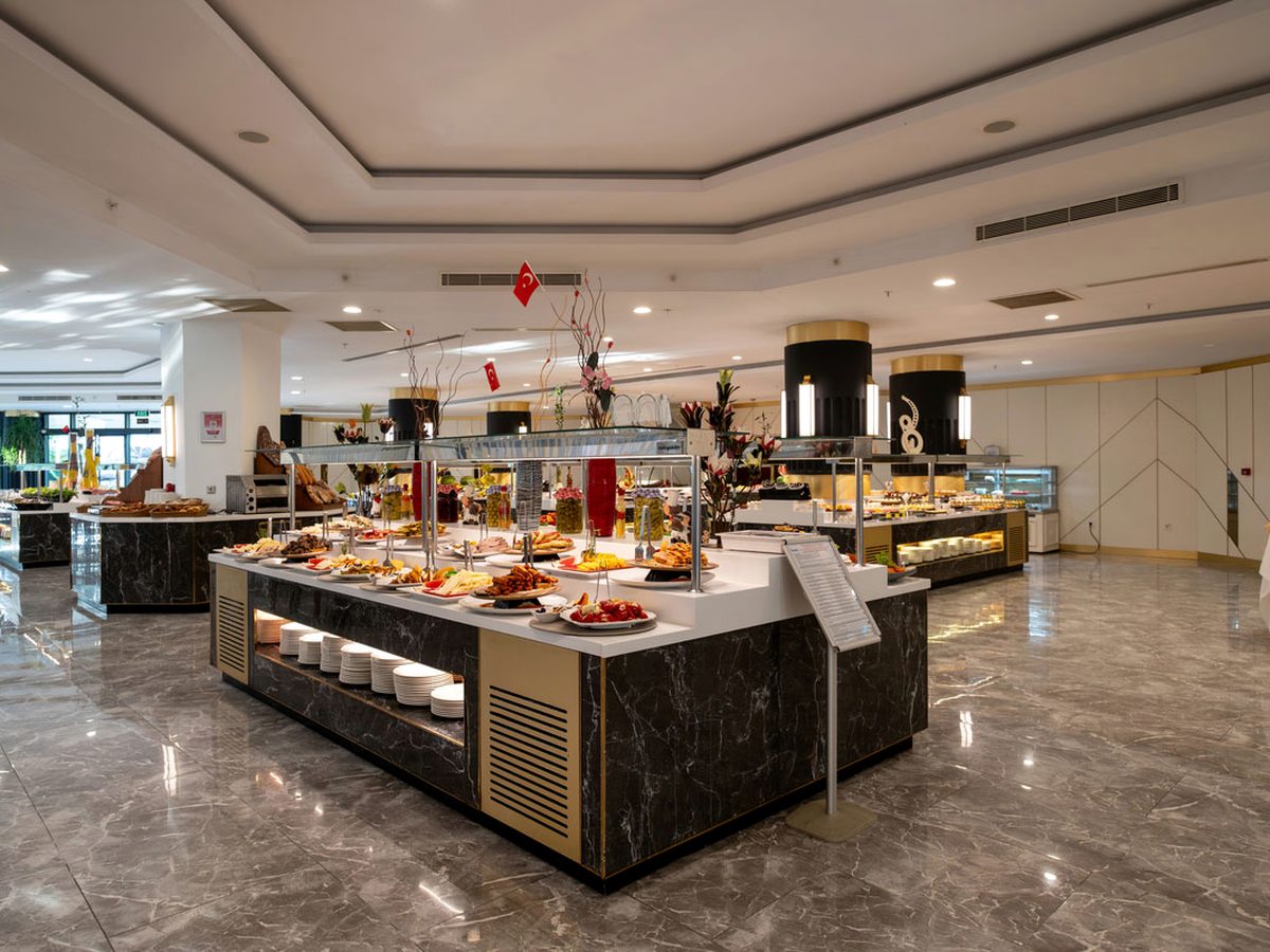 Buffet hall with black marble and gold serving islands laid with hot dishes and desserts, on a polished grey marble floor.