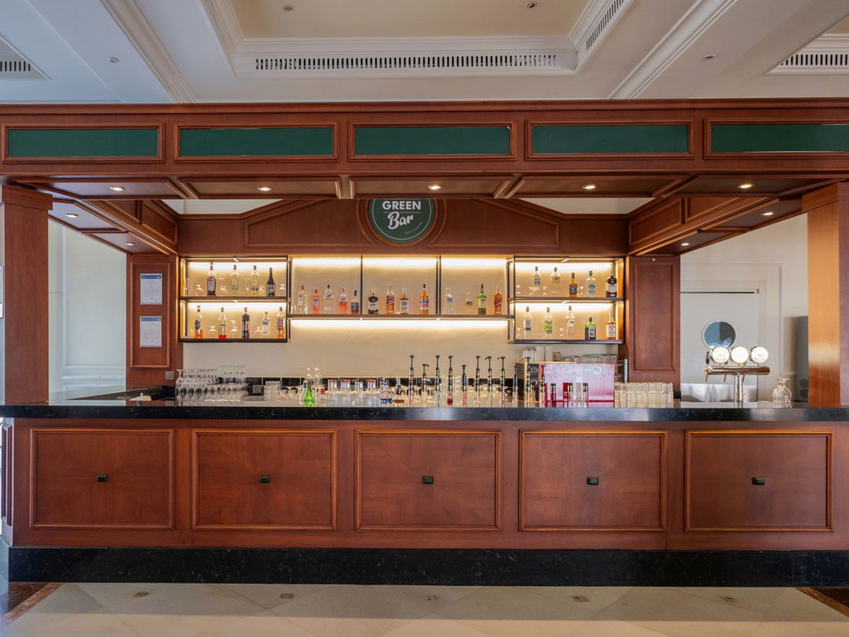 Indoor bar with a long wooden counter, backlit bottle shelves and beer taps.
