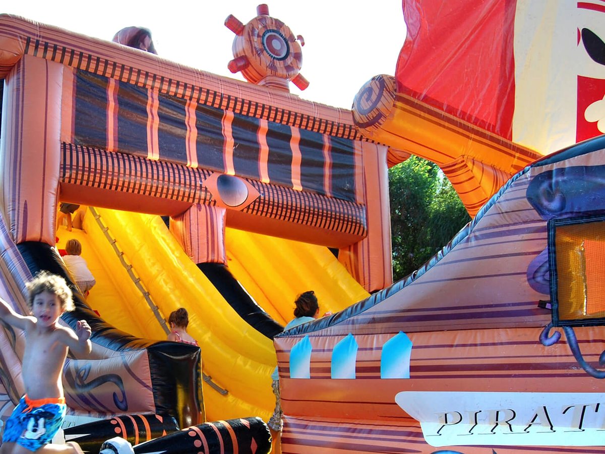 A brightly painted inflatable pirate galleon with a yellow slide, children climbing on it in the sunshine.