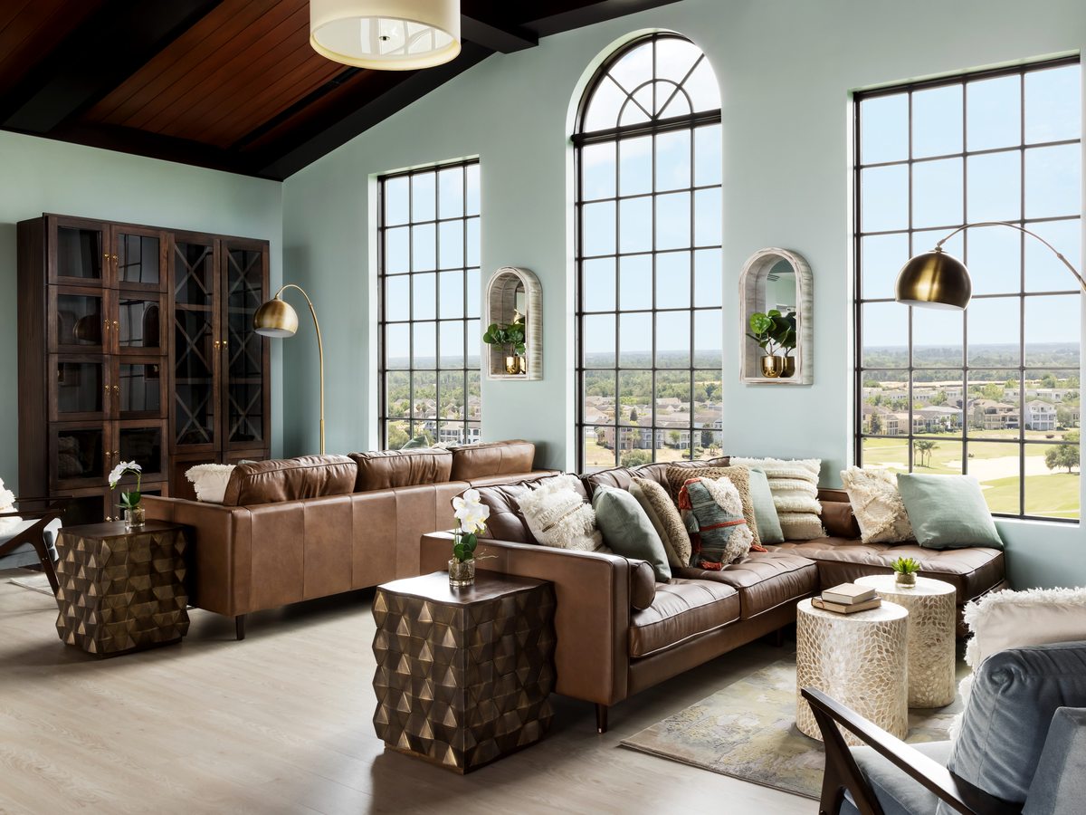 A villa living room with a high vaulted timber ceiling, a tall arched window, leather sofas, coffee tables and wood-effect flooring filled with natural light.