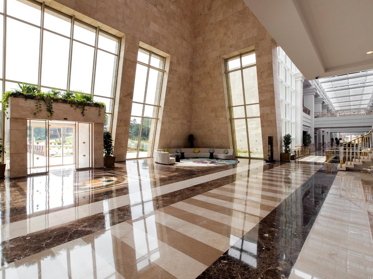 A tall, light-filled lobby with a glazed roof, full-height windows, a polished marble-effect floor and planters along the walkway.