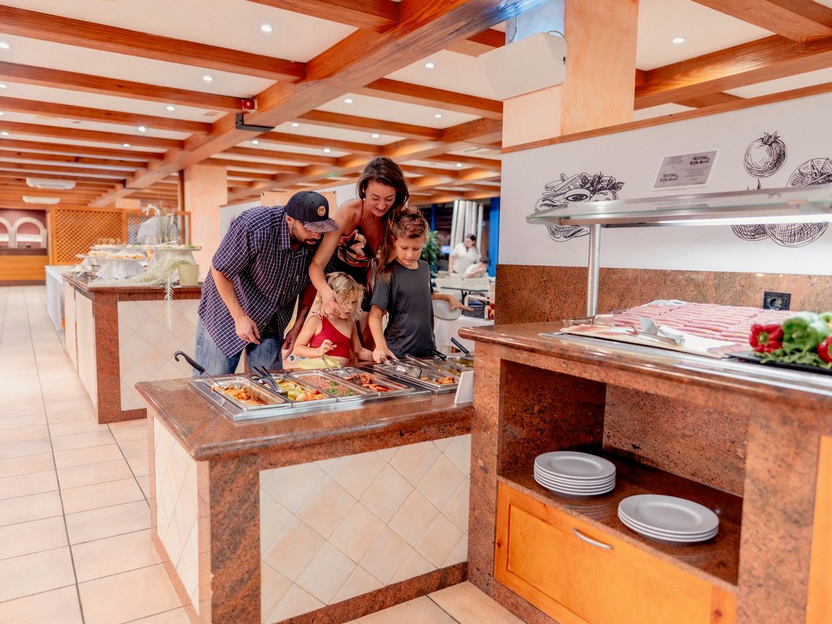 A buffet counter with trays of food under a glass screen and a family serving themselves on to plates.