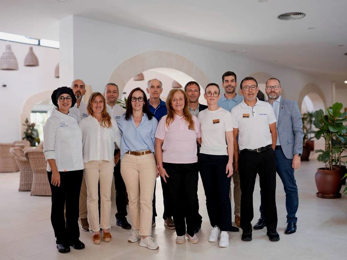 A group of uniformed hotel staff standing together in a bright reception area with white arched openings.