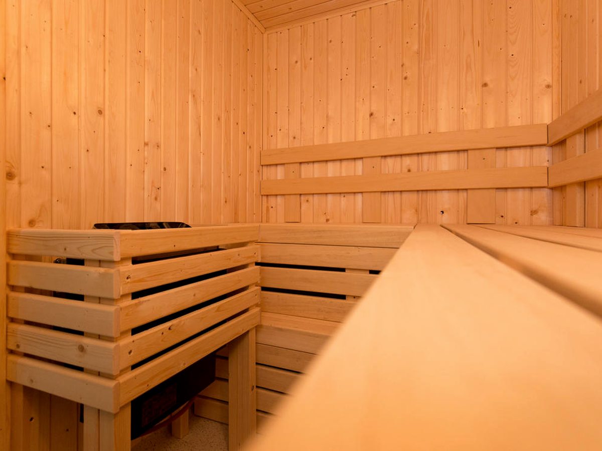 A small timber sauna with slatted wooden benches on two levels and a guard around the heater.