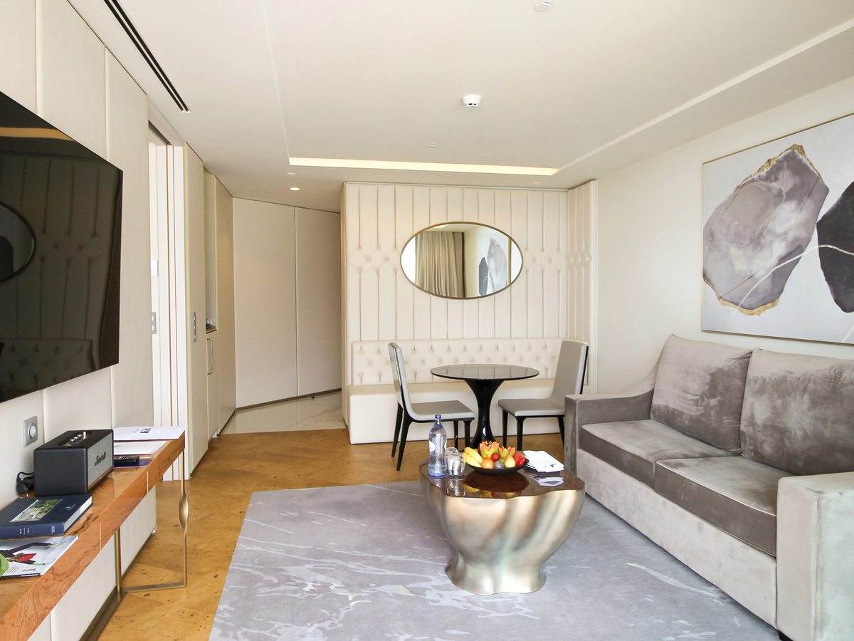 A suite living room with a grey sofa, a metal coffee table, a wall-mounted television and a round dining table with two chairs.