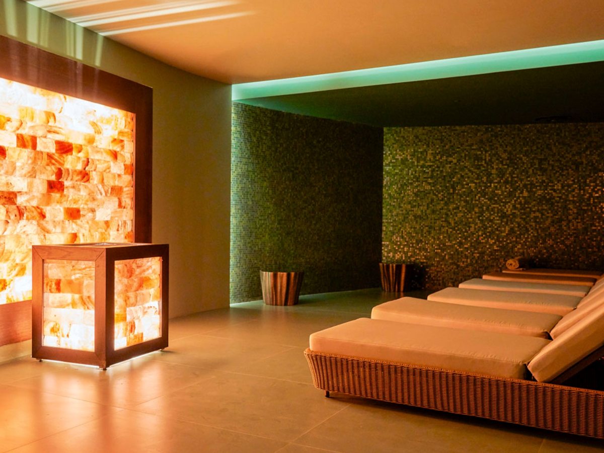 A warm-lit room with a backlit wall of salt bricks, a salt-block lantern and a row of cushioned wicker loungers.