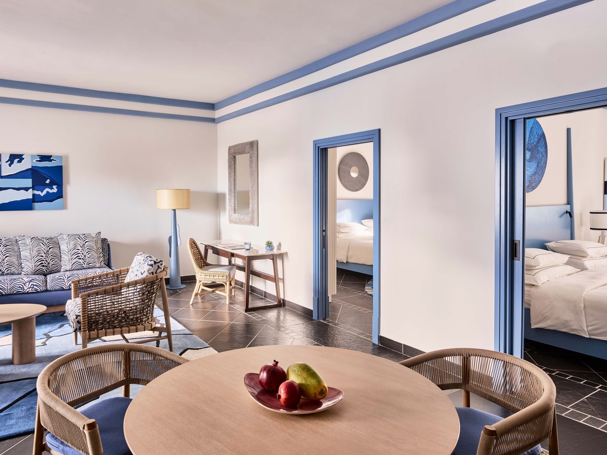 Suite living and dining area with a round wooden table and cane chairs, and open doorways through to the bedrooms.