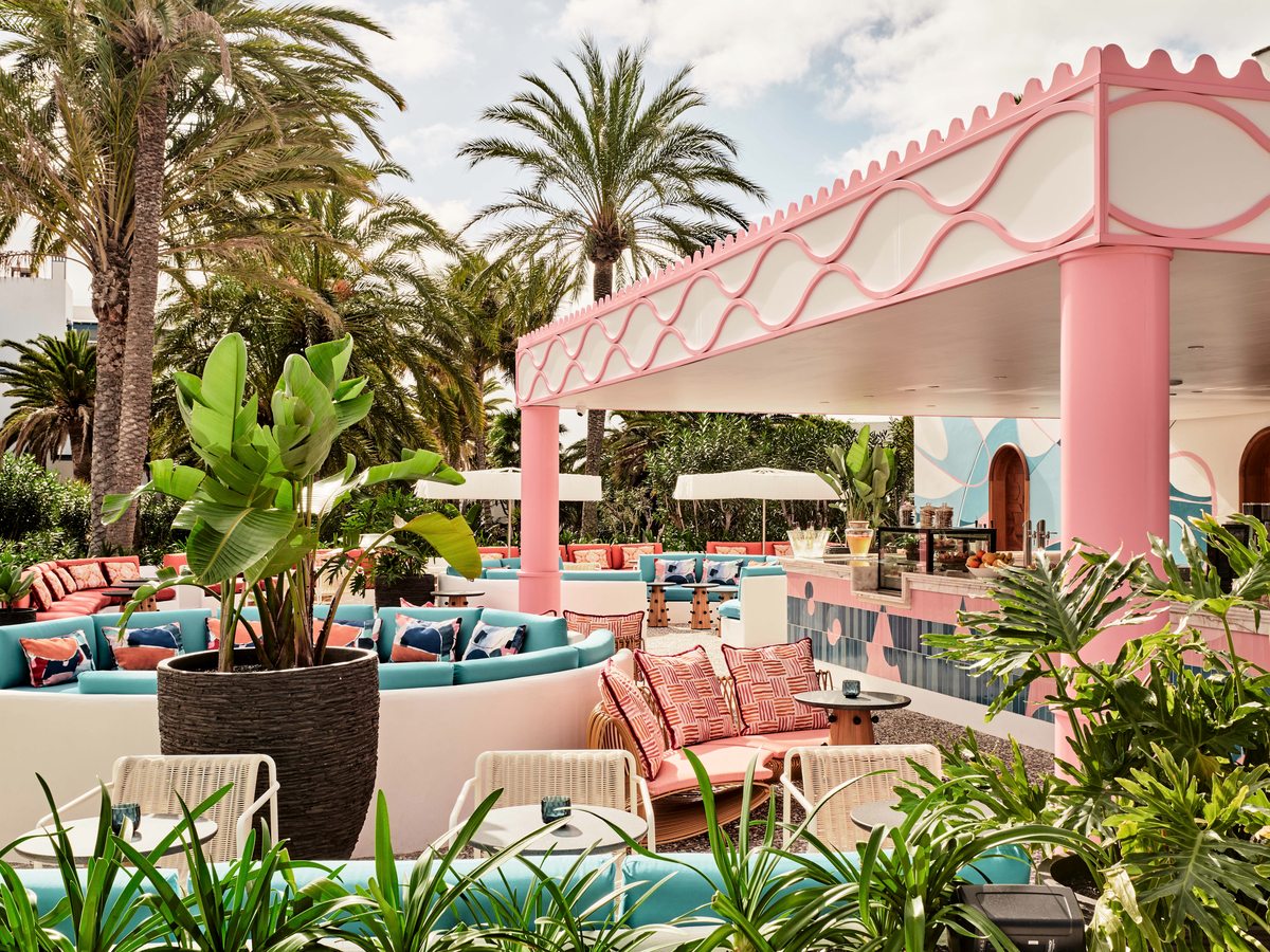 Poolside lounge under a scalloped pink canopy, with curved turquoise and coral banquettes, cane chairs and tropical planting.