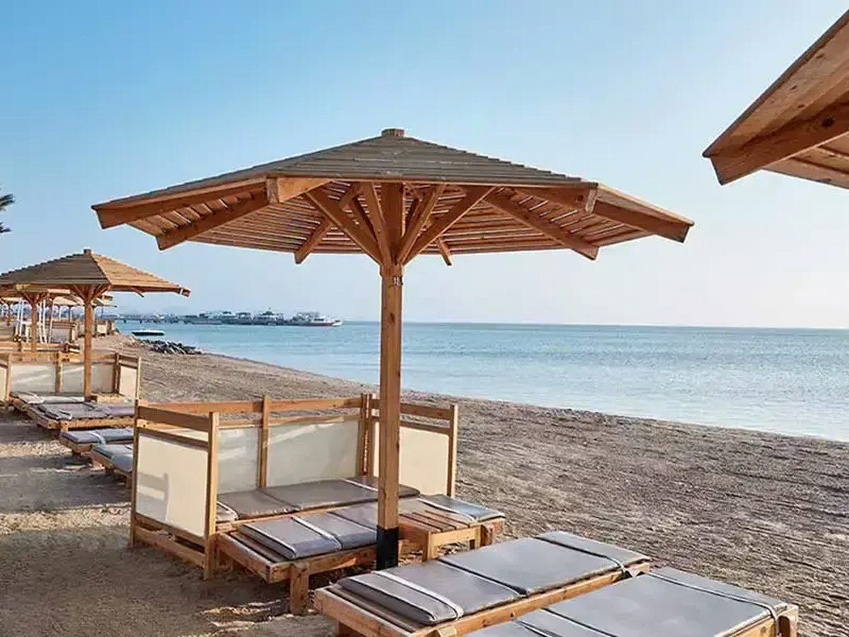 A row of wooden parasols and sun loungers on a sandy beach beside calm blue sea.