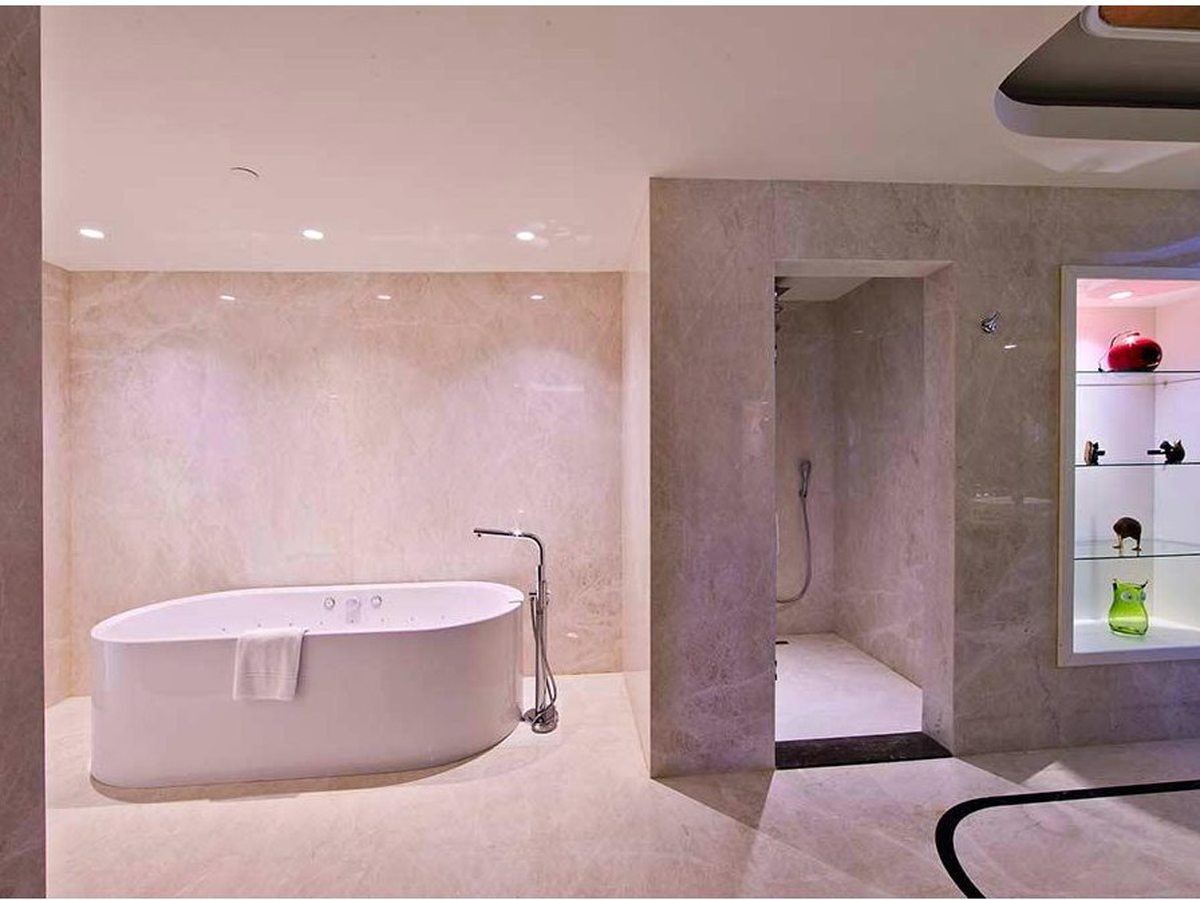 A stone-lined bathroom with a freestanding oval bath, a walk-in shower behind a partition and a lit display niche.