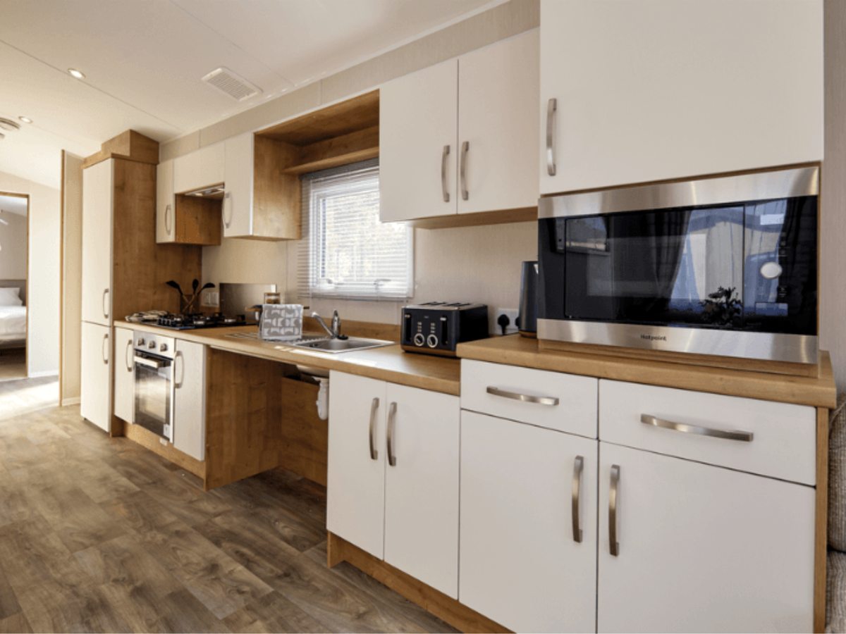A caravan kitchen with white units, wood-effect worktops, a gas hob, an oven, a microwave and a window over the sink.