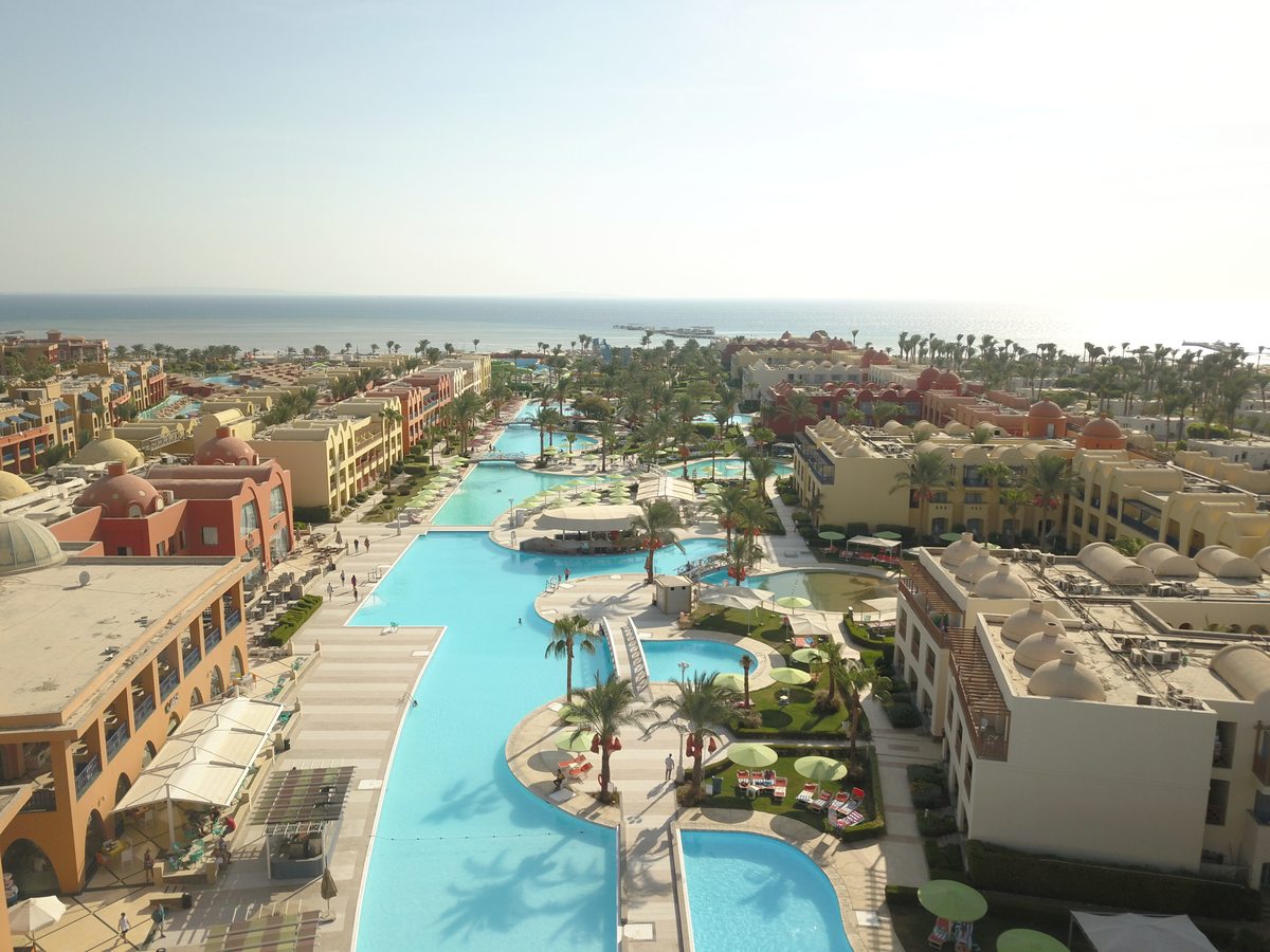 An elevated view along a long turquoise pool winding between terracotta and cream guest buildings towards the Red Sea.