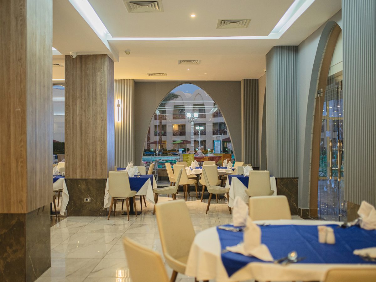 A restaurant dining room set for service with blue tablecloths, folded napkins, beige chairs, columns and arched windows.