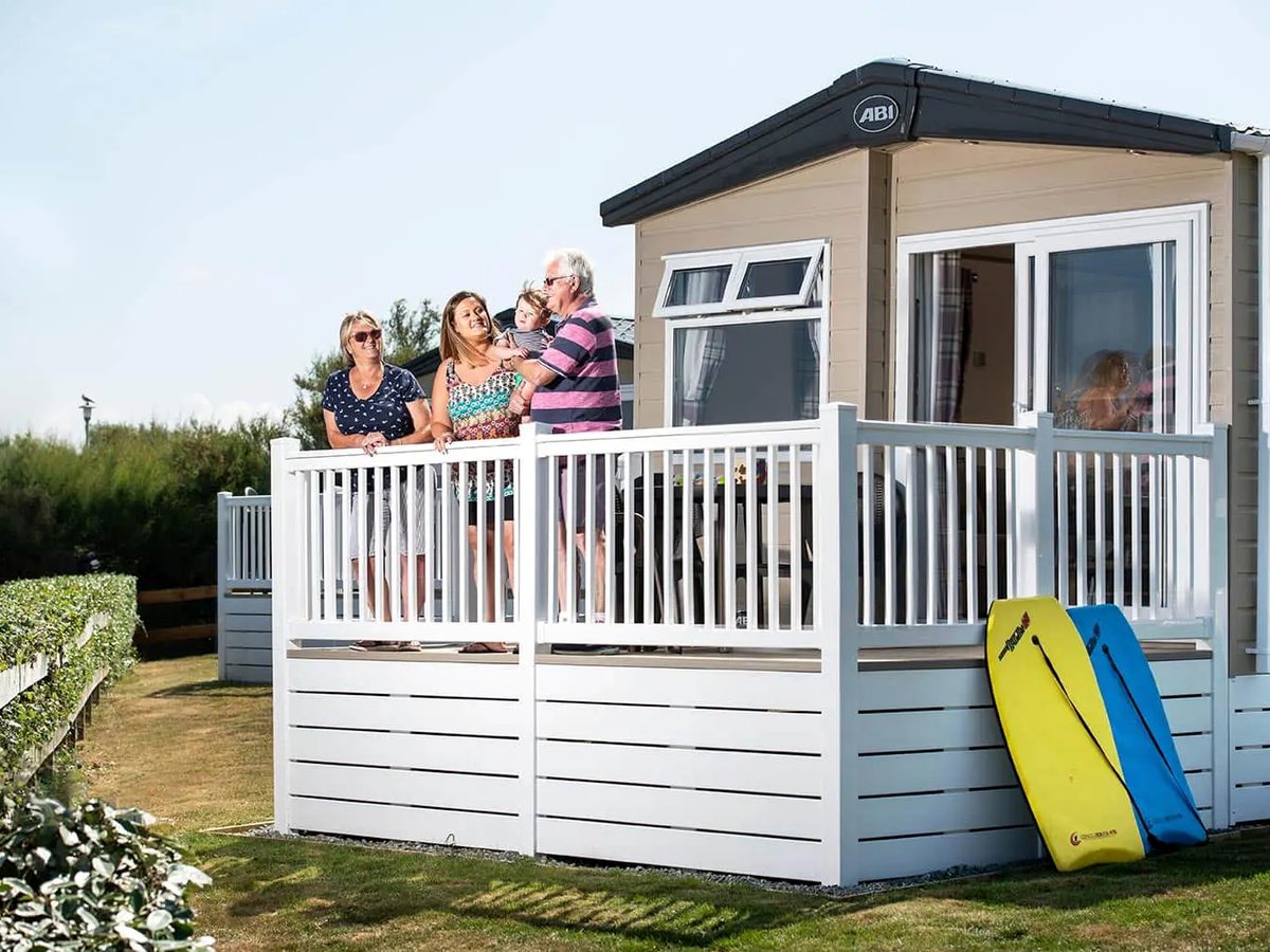 A family standing on the white decking of a cream static caravan, with two bodyboards propped against the deck.