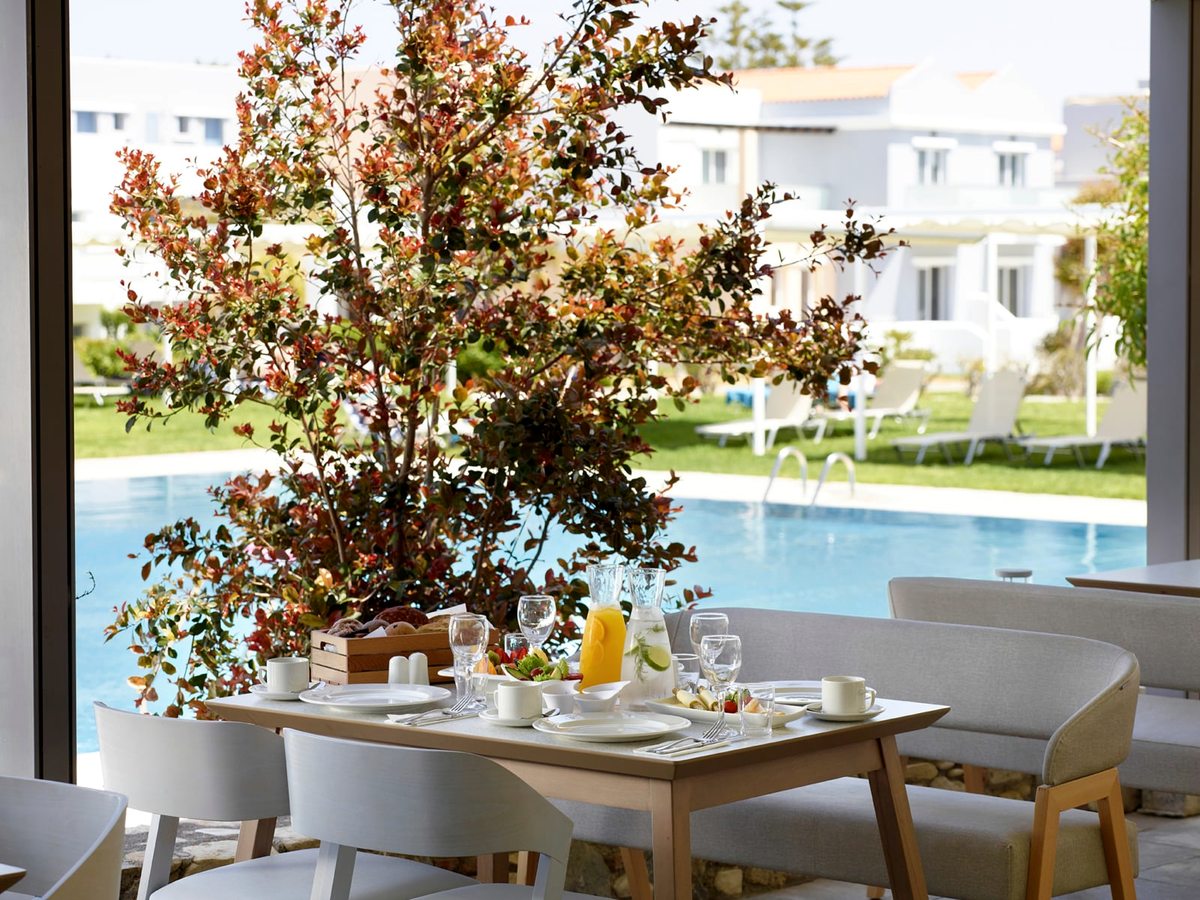 Table laid for breakfast with pastries, fruit, juice and coffee beside an open wall looking onto the pool and lawns.