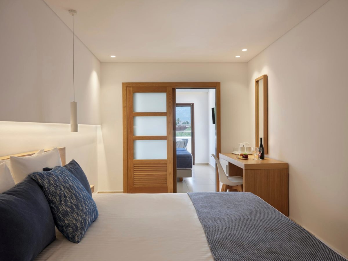 Suite bedroom with a double bed, navy and grey cushions, a pendant bedside light and an open sliding wooden door through to a second bedroom.