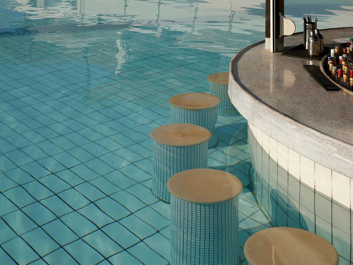 Curved poolside bar counter with submerged stools in turquoise water and bottles lined up along the counter.