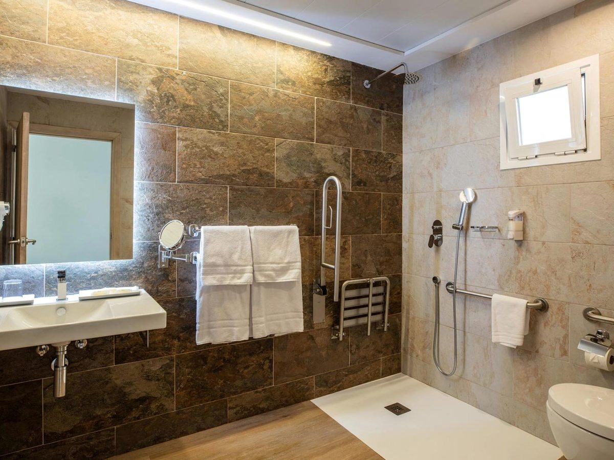 An adapted bathroom with a level-entry shower, grab rails, a fold-down shower seat and a basin with a mirror above.