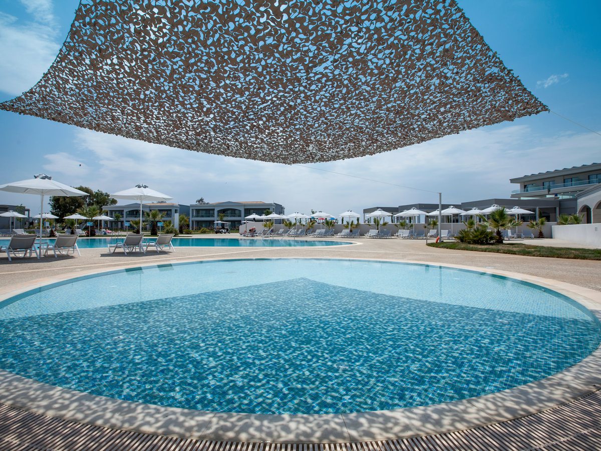 A circular shallow pool with a timber deck around it, a large woven shade canopy over the deck, and a larger pool, loungers and parasols behind.