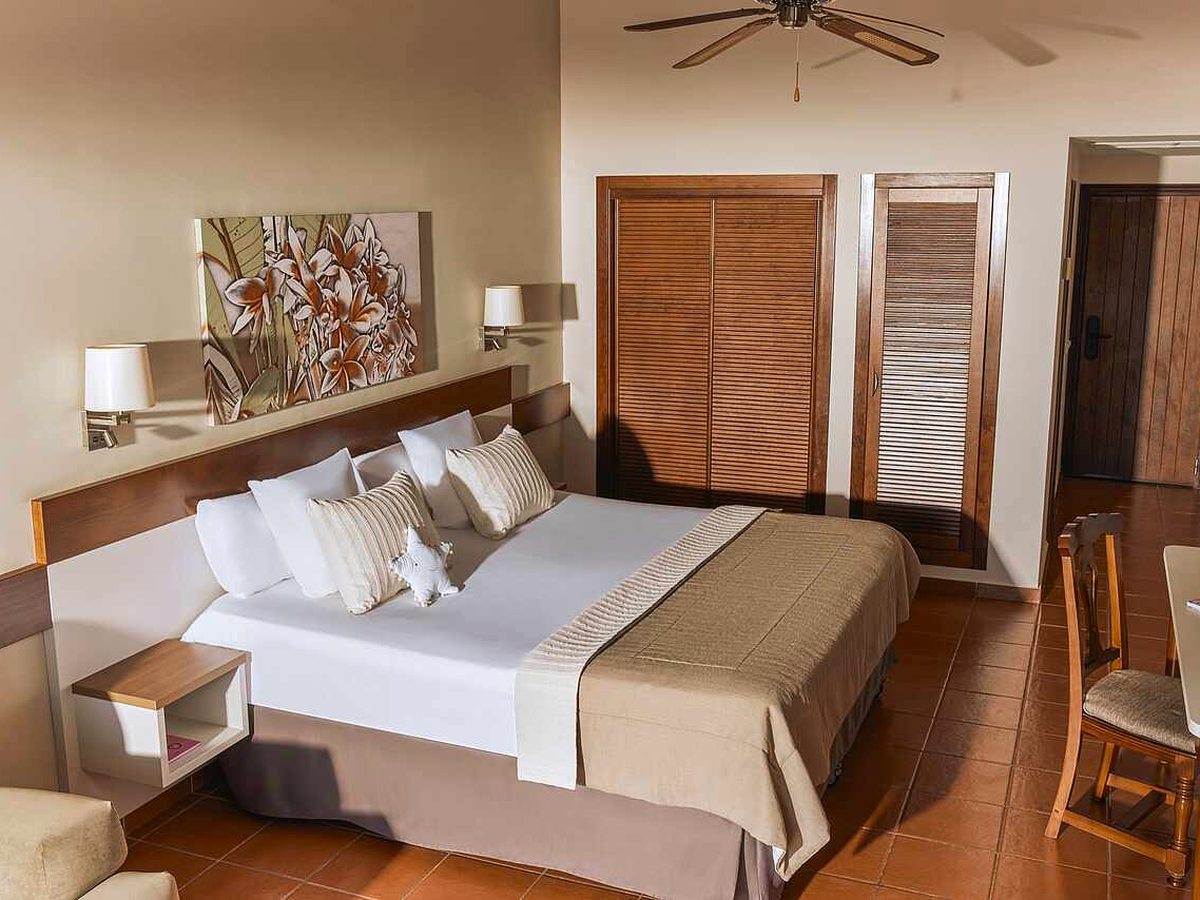 Hotel bedroom with two single beds pushed together under a wooden headboard, a louvred wooden wardrobe, a ceiling fan and terracotta floor tiles.