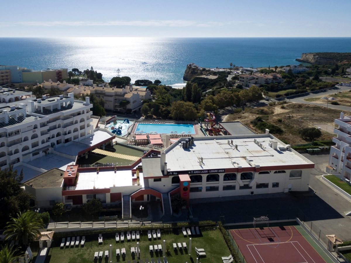 Aerial view over the resort's leisure building, its rectangular pool and water slides, with the coast and open sea beyond.
