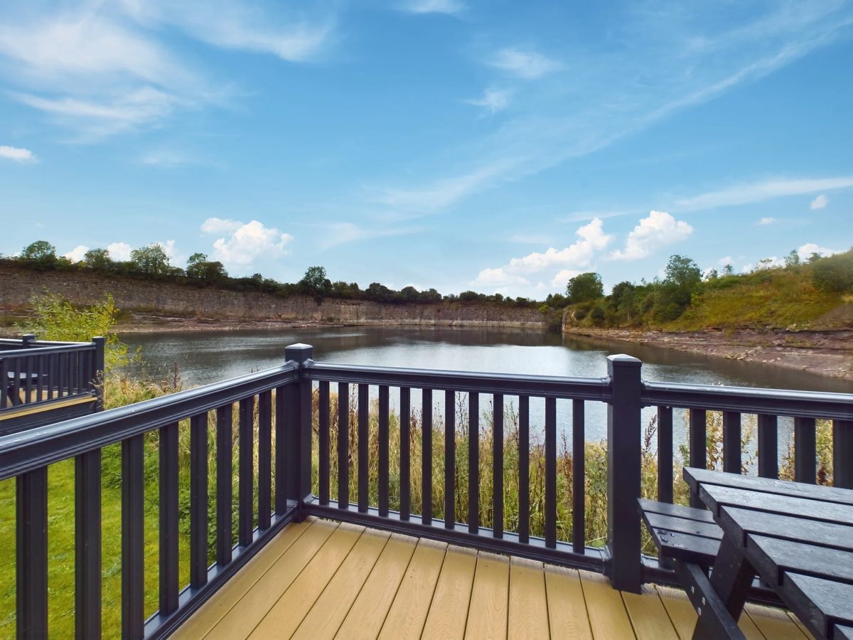 A composite timber deck with a picnic table and a dark balustrade above the still quarry lake, with the quarry's rock banks on the far side.