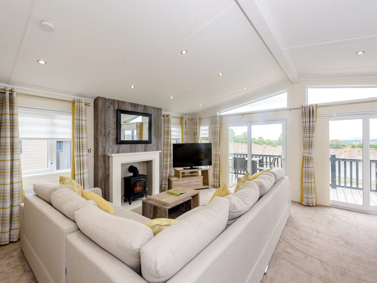 A lodge lounge with two cream sofas, a television above a fireplace, coffee tables and glazed doors onto the deck.
