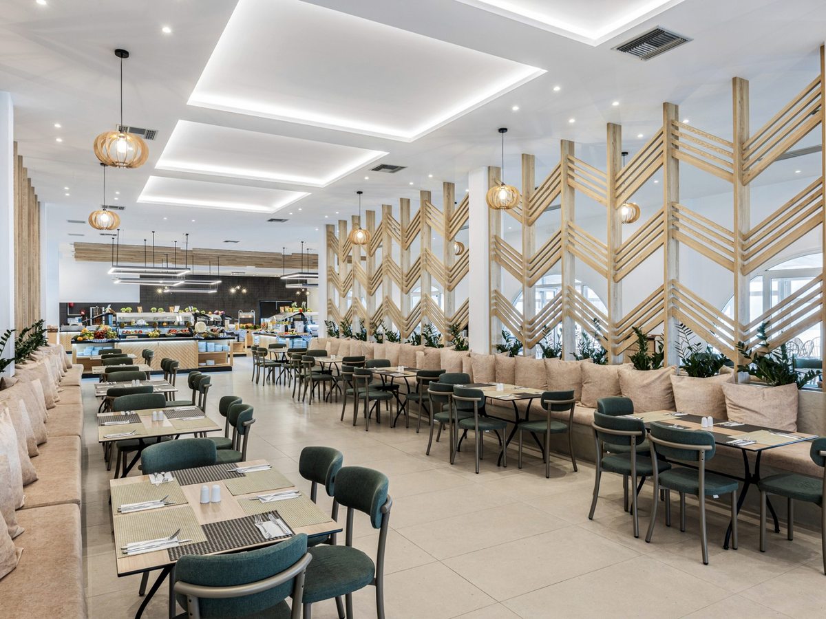 Indoor restaurant with green upholstered chairs, cushioned banquettes and laid tables between chevron timber screens, with the buffet counters at the far end.