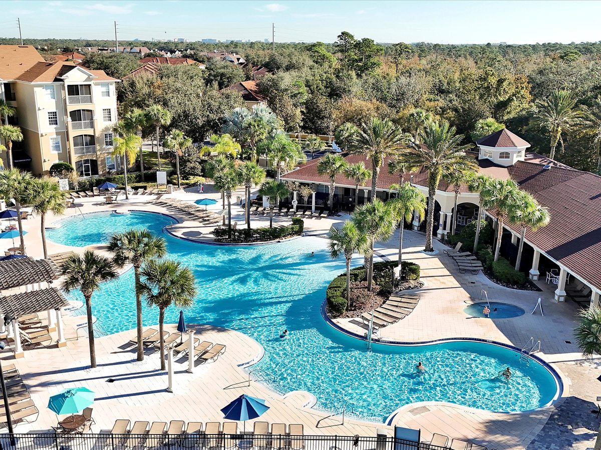 Elevated view of a freeform blue pool and water-play area surrounded by resort buildings and palm trees.