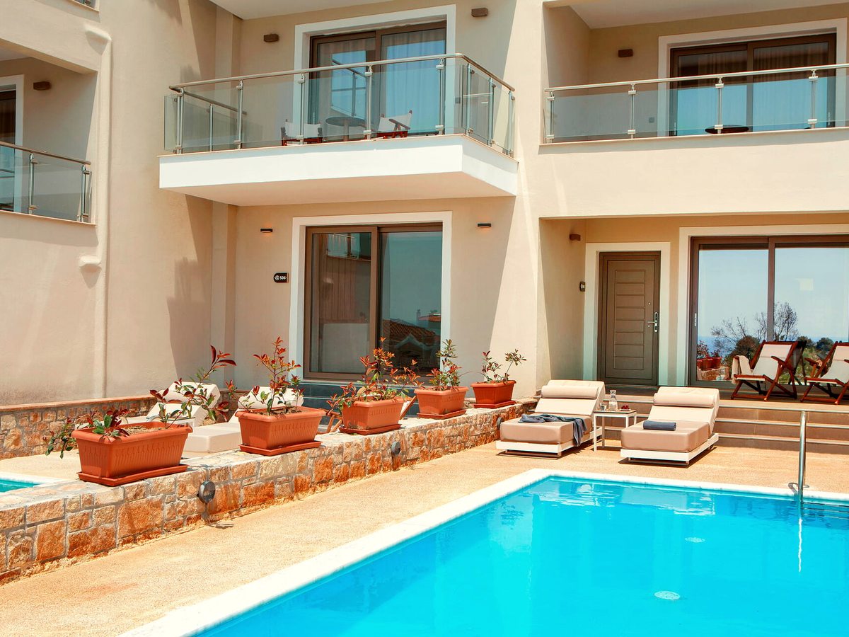 A rectangular pool below a two-storey accommodation block, with sun loungers on the terrace and terracotta planters along a low stone wall.